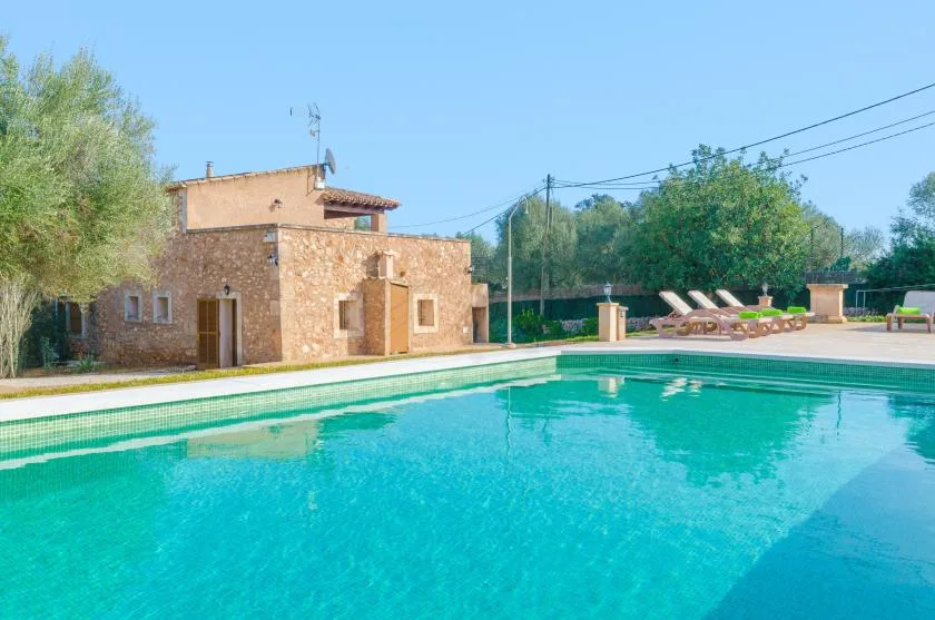 Una piscina junto a un edificio de piedra y asientos de descanso.