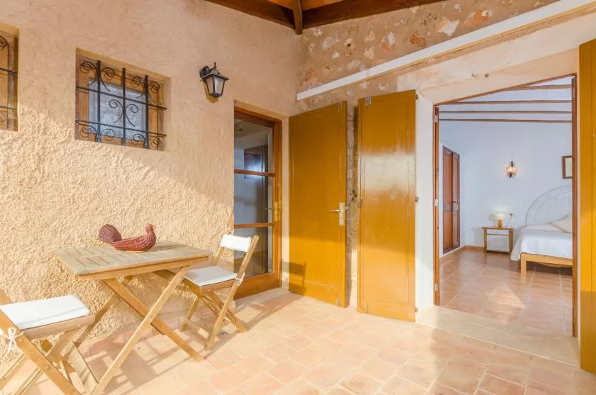Un patio interior rústico tiene una mesa pequeña y asientos junto a una puerta abierta.