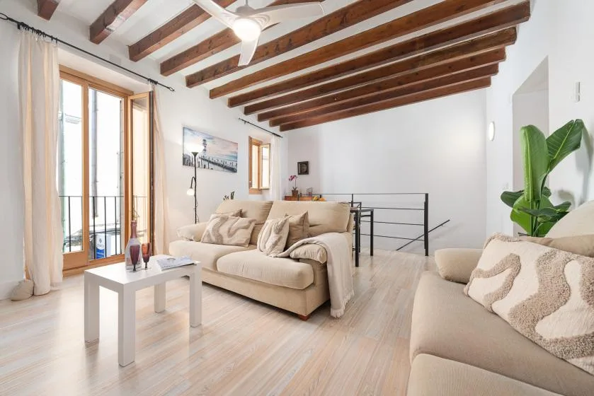 A bright living room with beige seating, a coffee table, and exposed ceiling beams.