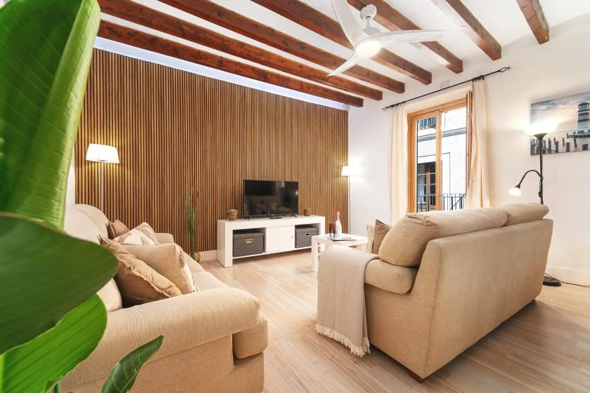 A bright living room with beige seating, a television, and exposed ceiling beams.
