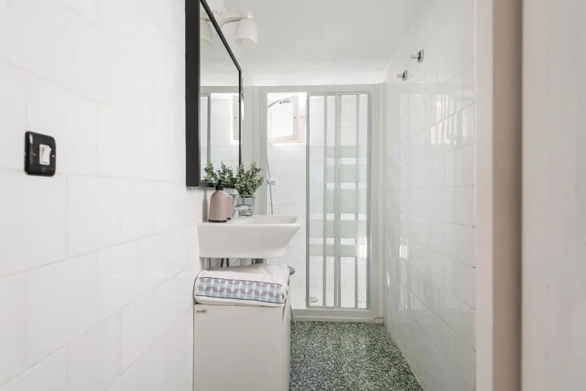 A bright tiled bathroom with a sink and frosted glass shower doors.