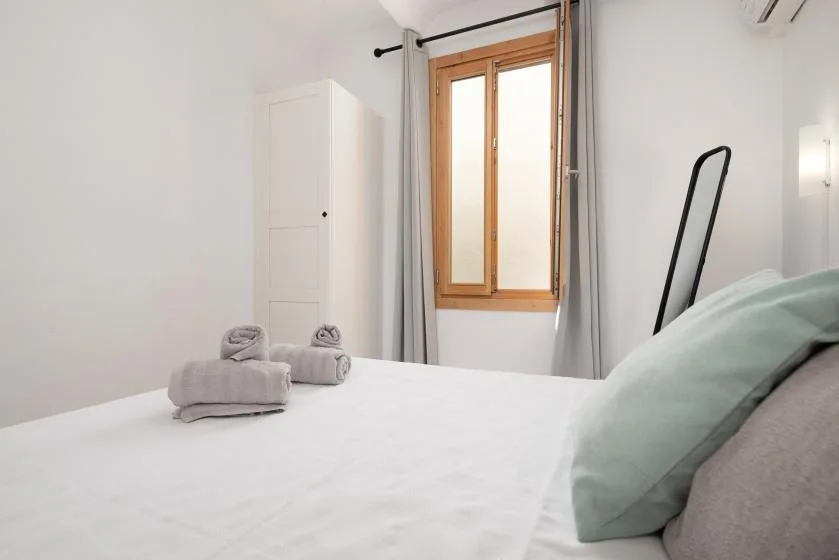 A bright bedroom with a neatly made bed and a wooden-framed window.