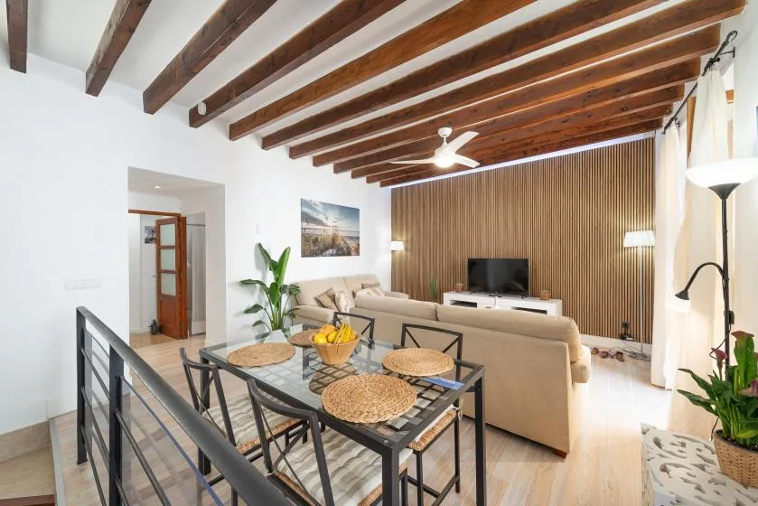 A dining area opens onto a living room with a television and exposed ceiling beams.