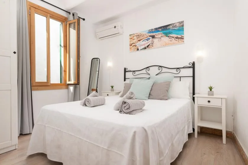 A bright bedroom with a white bed, pale pillows, and a window.