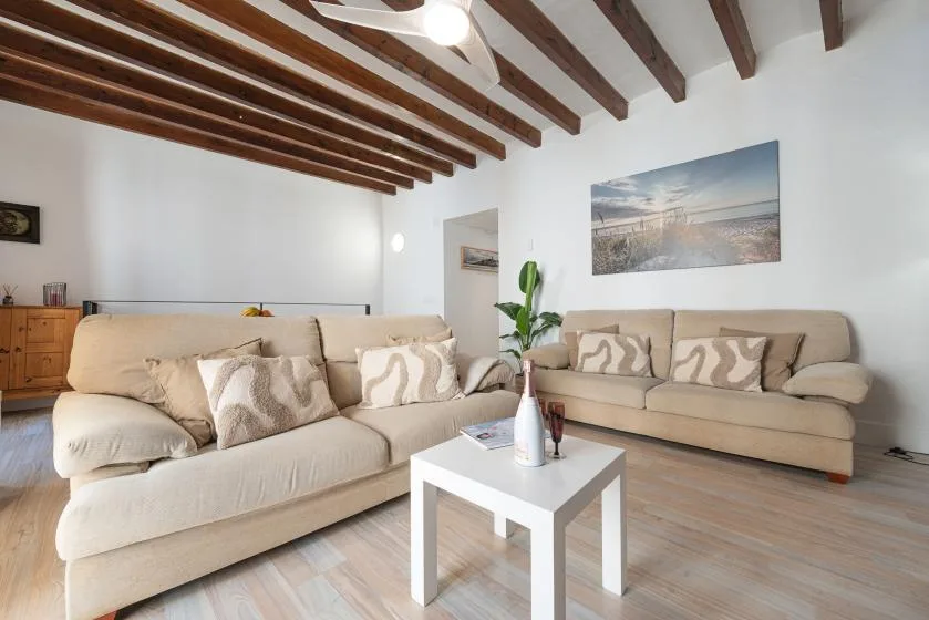 A living room with beige seating, a white coffee table, and exposed wooden ceiling beams.