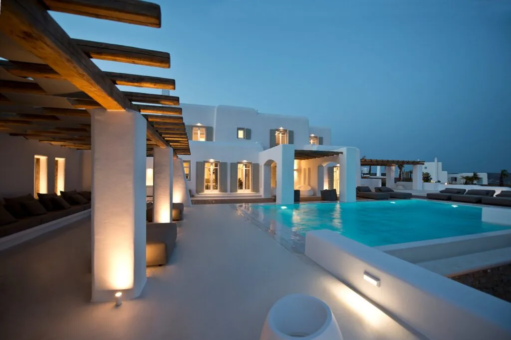Una villa moderna con piscina iluminada y zona de estar exterior cubierta.