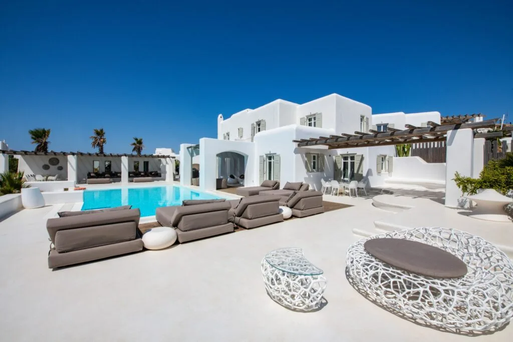 Un patio de villa blanca con piscina y asientos al aire libre.