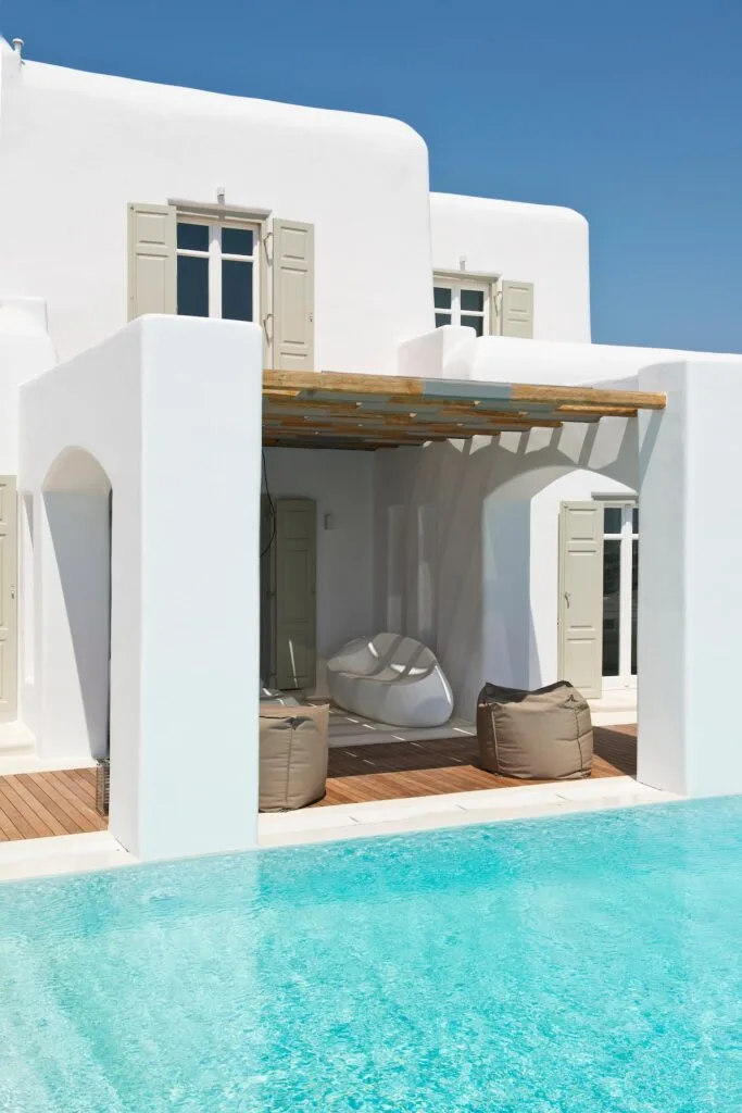 A white villa patio with shaded seating beside a turquoise swimming pool.