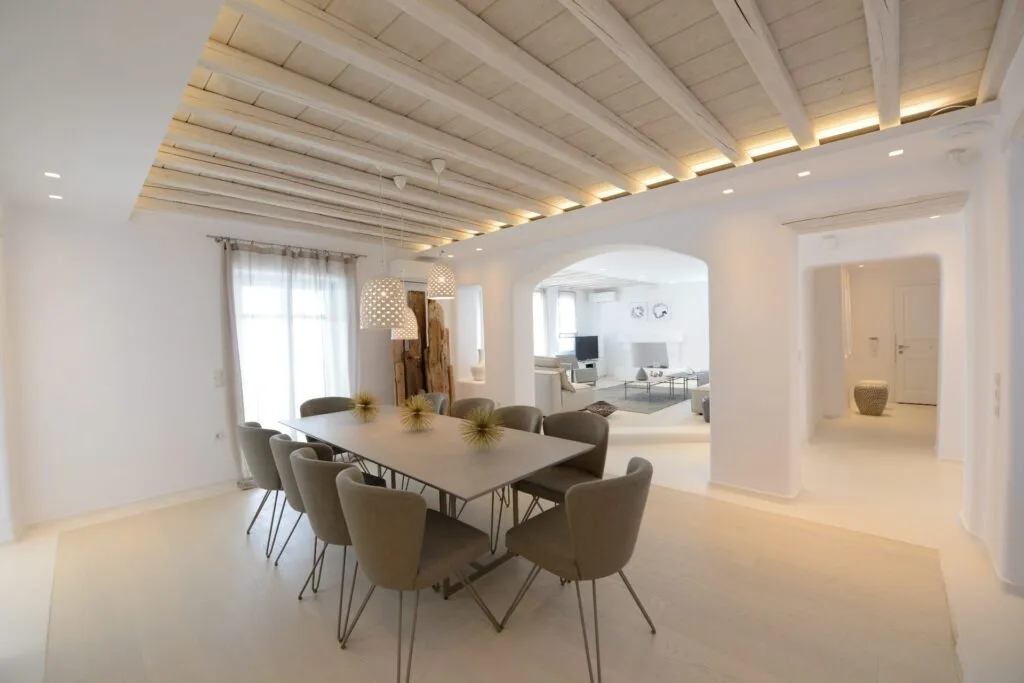 Un comedor luminoso con una mesa y asientos bajo un techo con vigas.