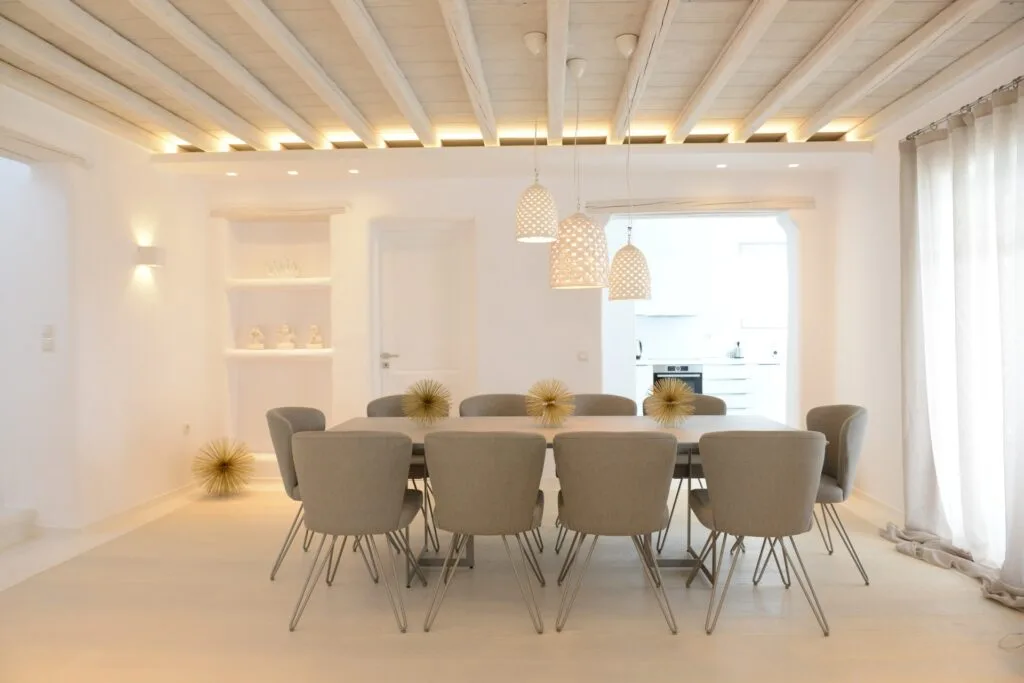 Un comedor luminoso con una mesa larga, asientos tapizados y lámparas colgantes.