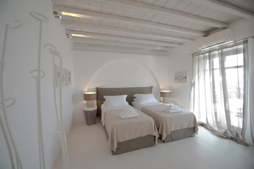 Un dormitorio luminoso con dos camas y una gran ventana con cortinas.