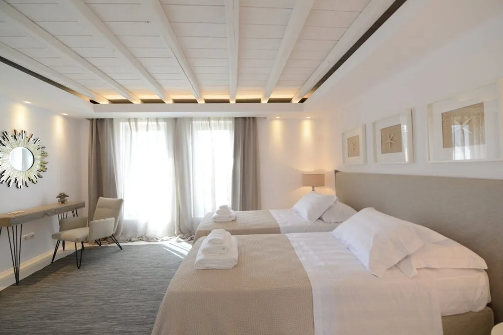 Un dormitorio luminoso con dos camas, un escritorio y cortinas translúcidas.