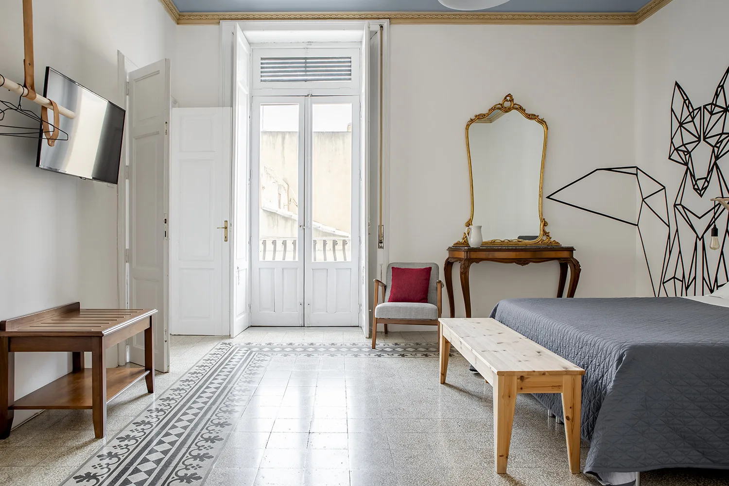 A bedroom with a bed, a small table, and a tall window.