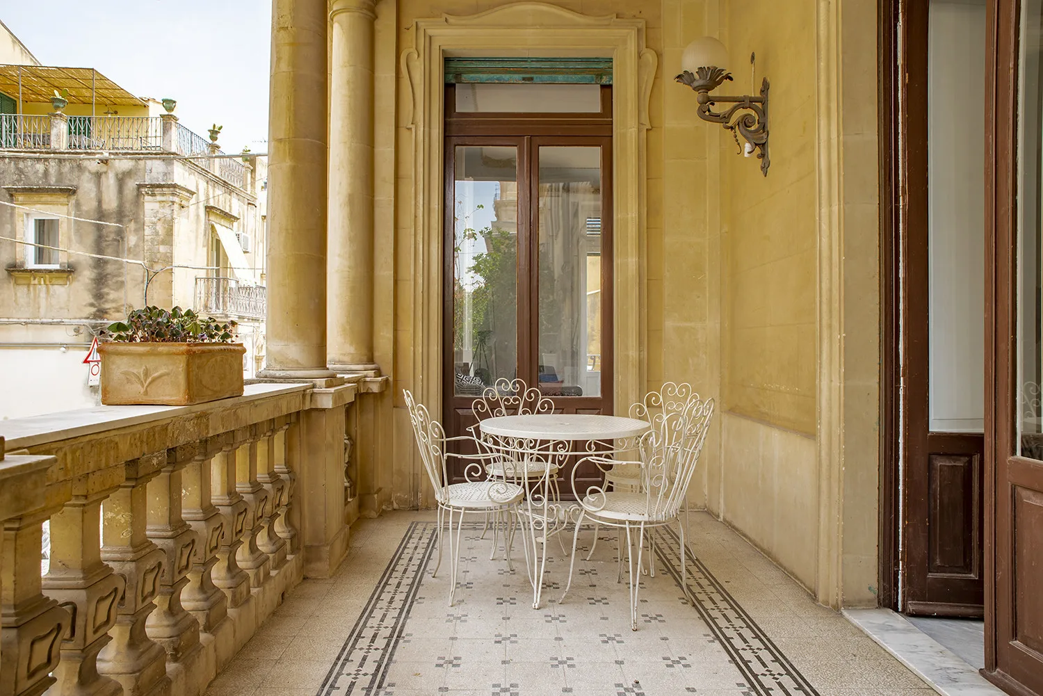 A balcony terrace with a small table and seating beside tall windows.