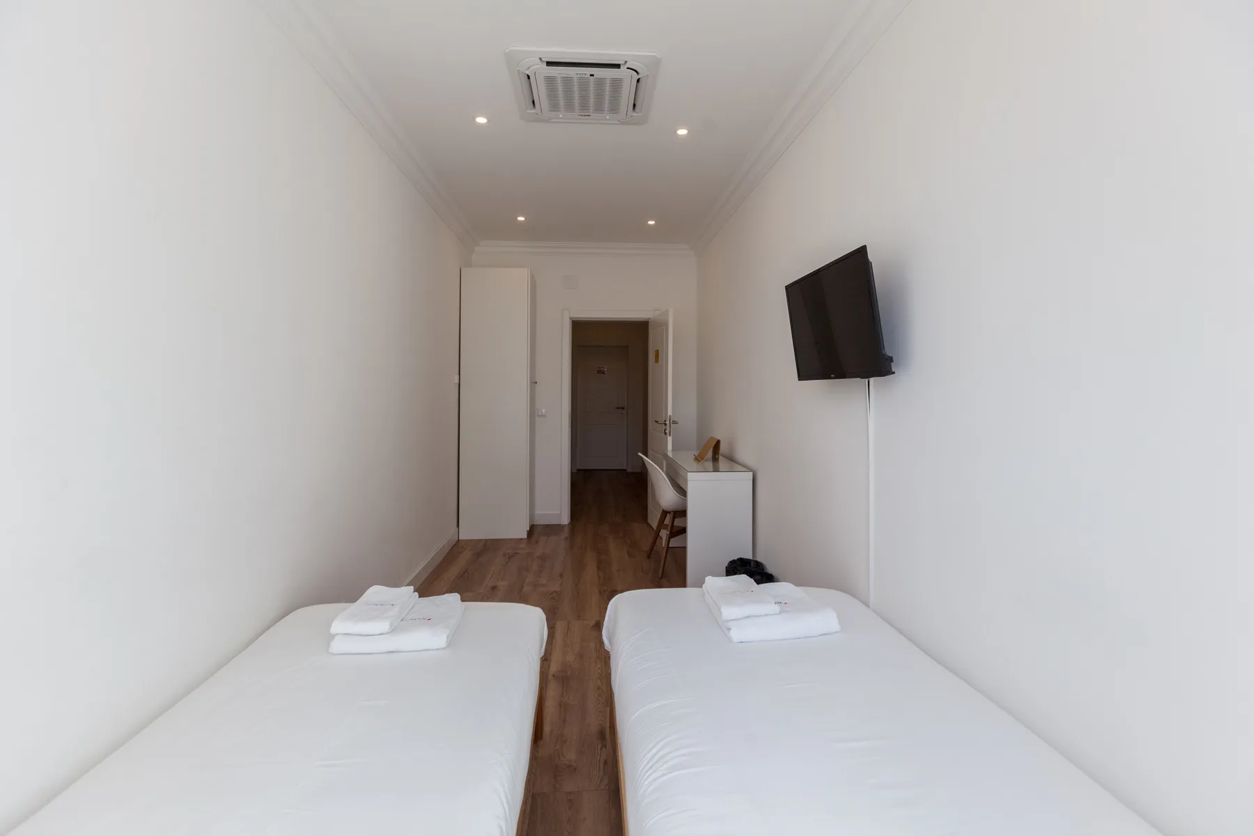 Un dormitorio luminoso con dos camas, un televisor en la pared y suelo de madera.