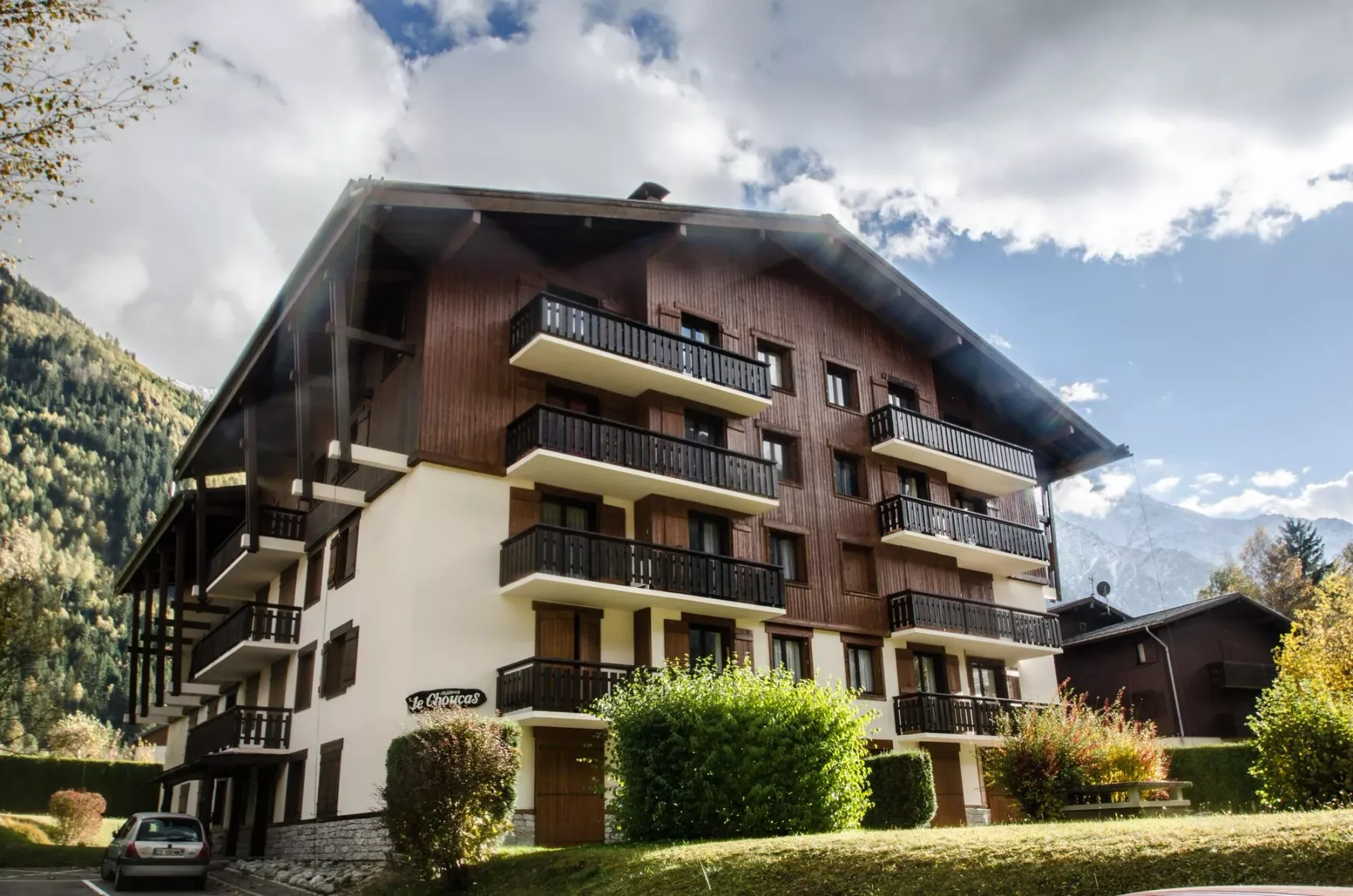 A multi-story chalet-style building with balconies stands against a mountain backdrop.