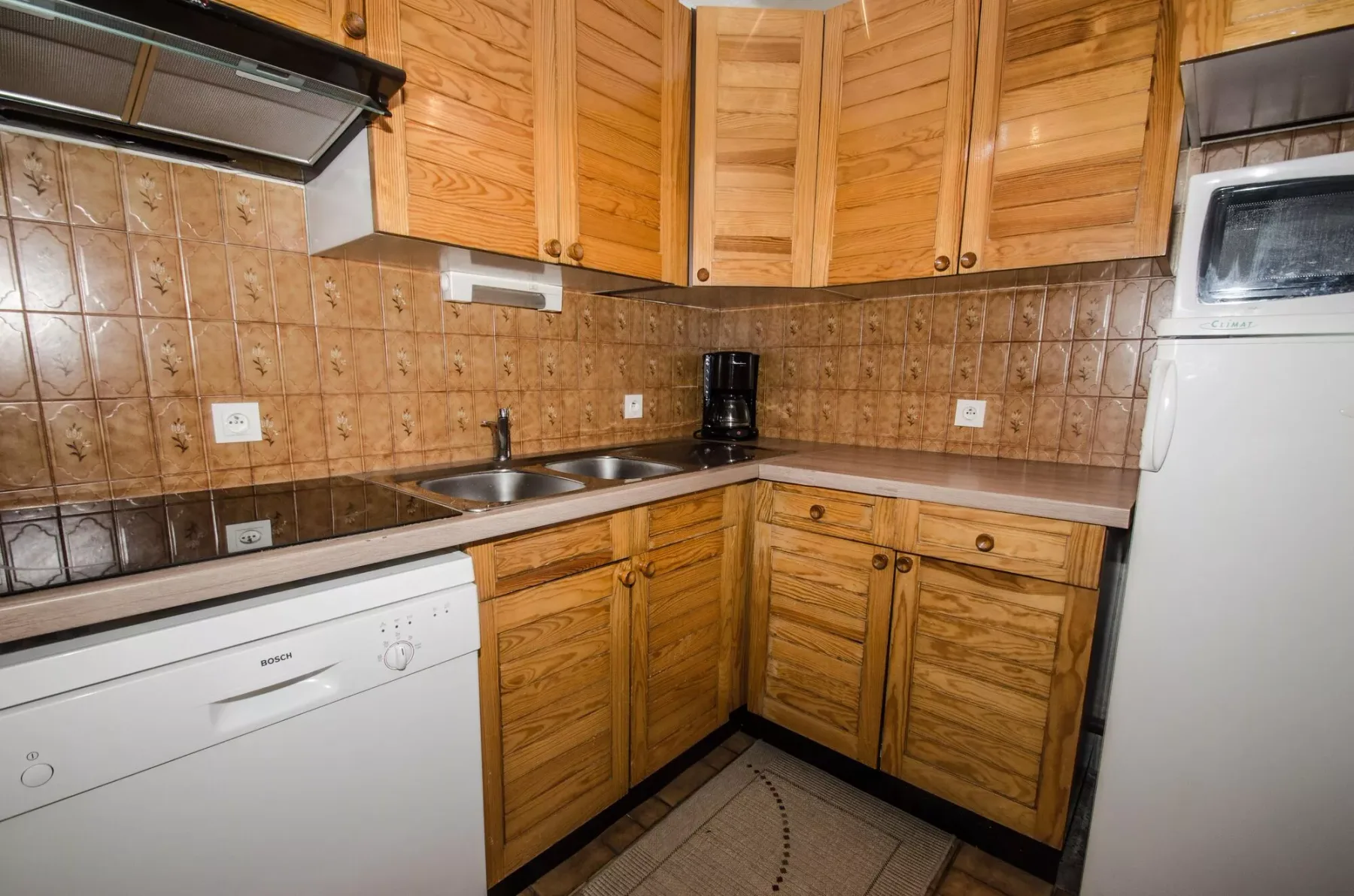 A compact kitchen with wooden cabinets, dark countertops, and built-in appliances.