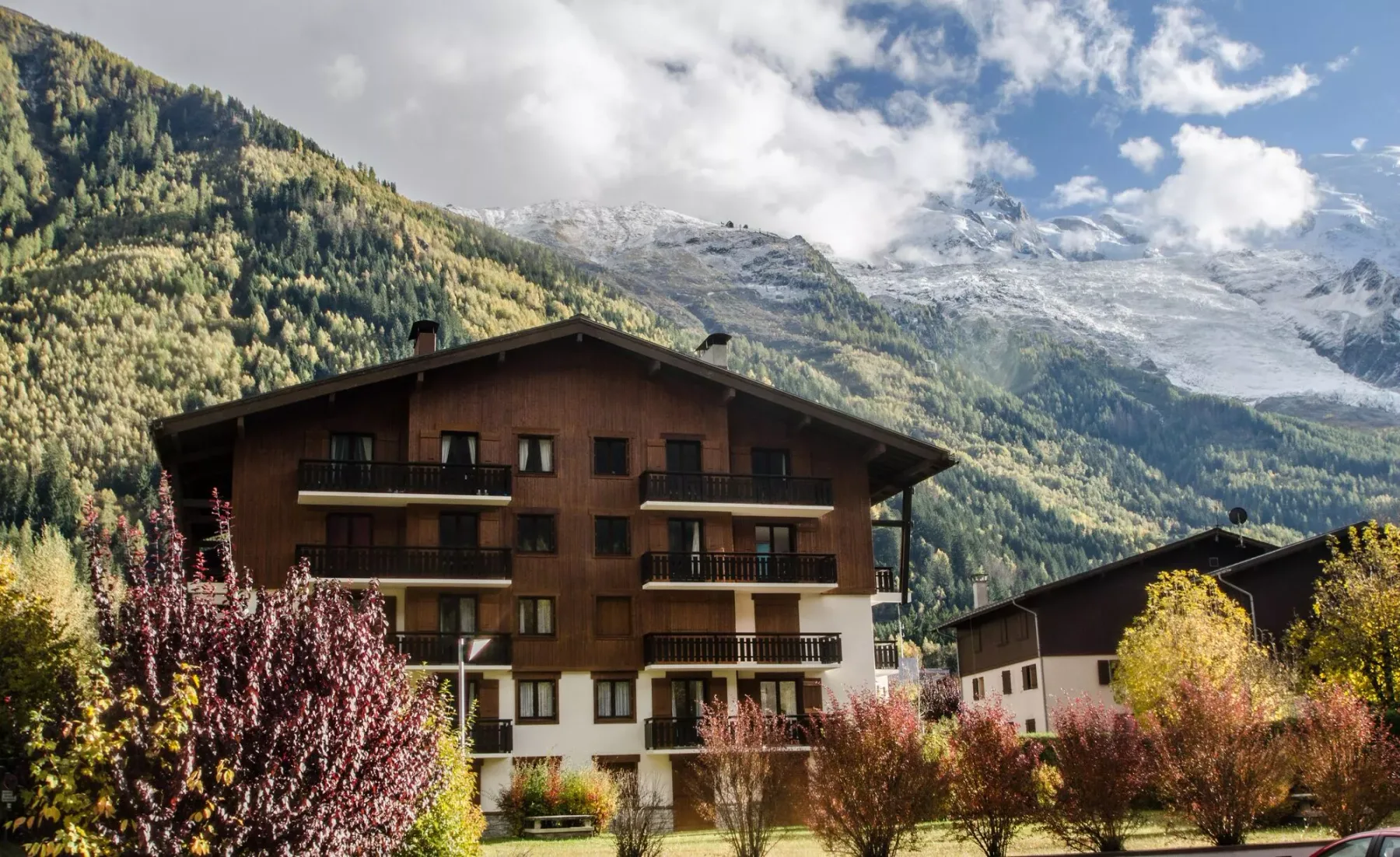 A brown multi-story building stands among trees beneath a mountain range.