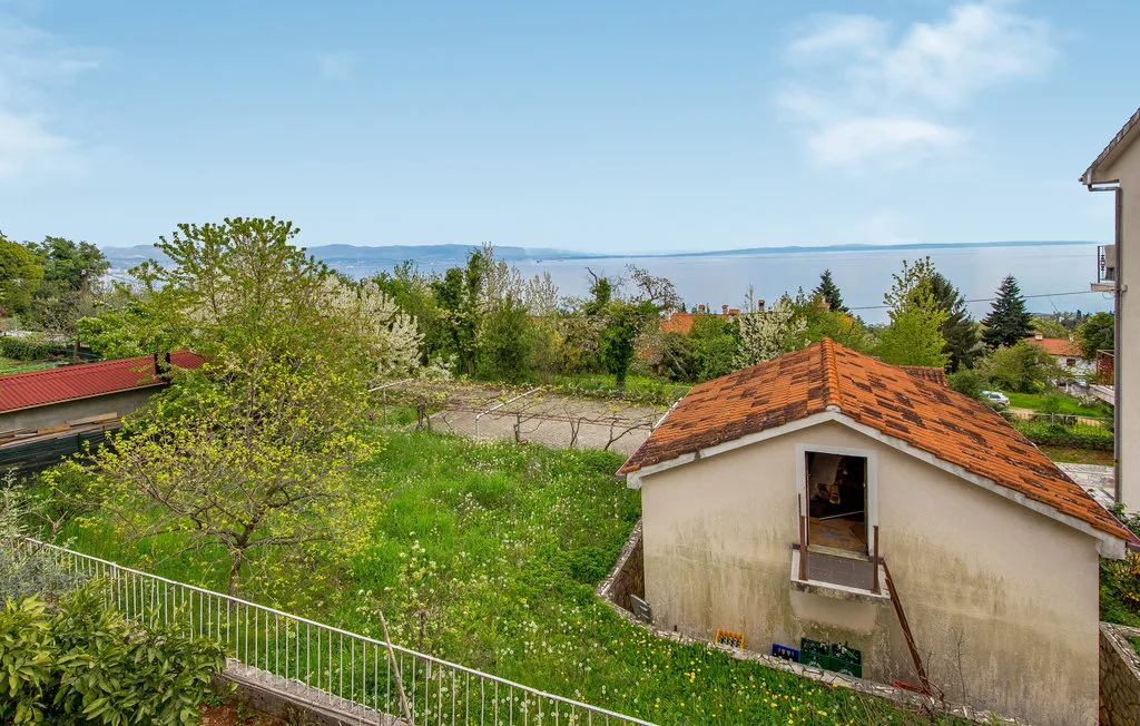 A small outbuilding stands in a green garden with water visible beyond the trees.