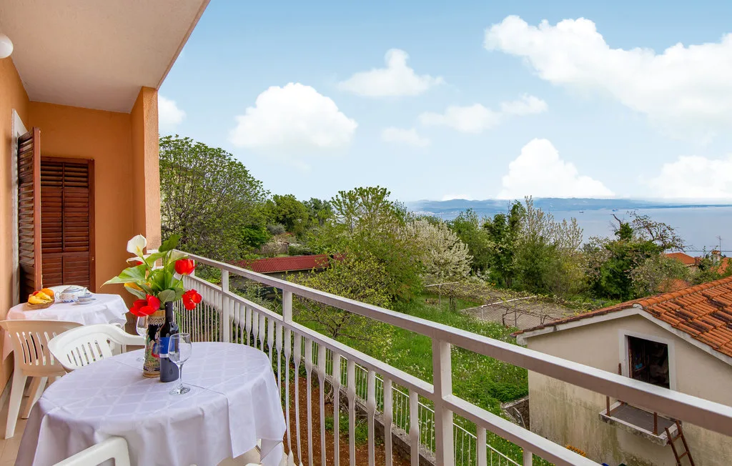 A balcony dining area overlooks leafy greenery and distant water.