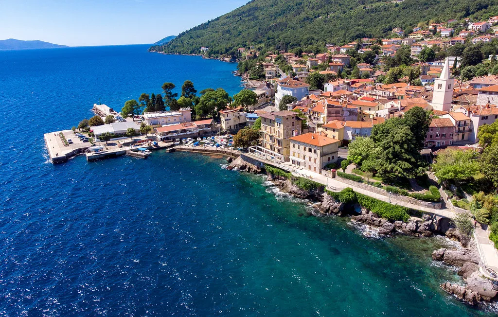 A coastal village sits beside a blue bay, with a waterfront harbor.