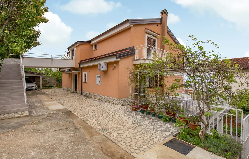 A peach-colored house stands beside a paved courtyard with potted plants.