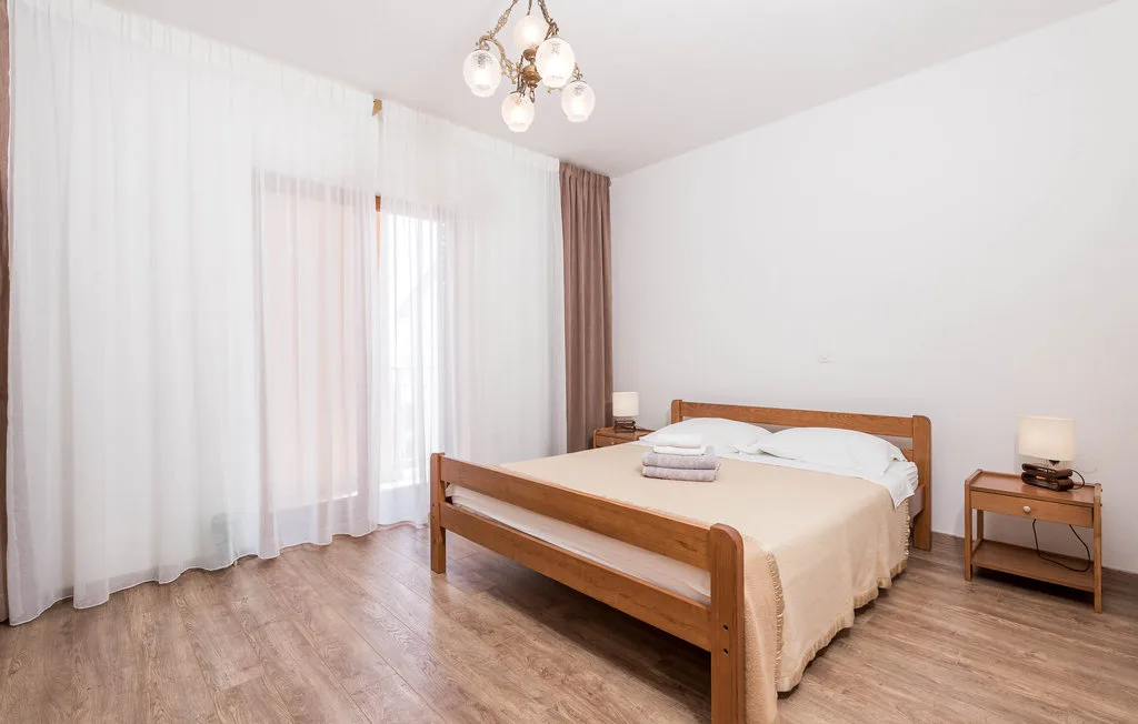 A bedroom with a wooden bed beside tall curtained windows.