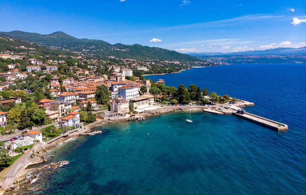 Coastal town along a blue bay, with hills rising behind the waterfront.
