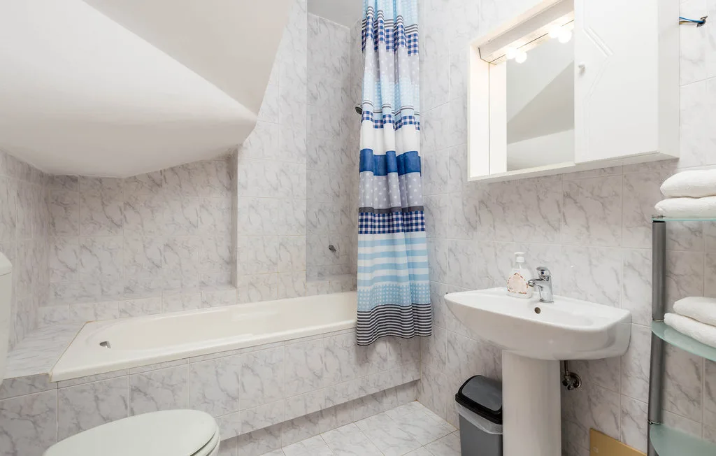 A marble-patterned bathroom with a bathtub, sink, and blue-striped shower curtain.