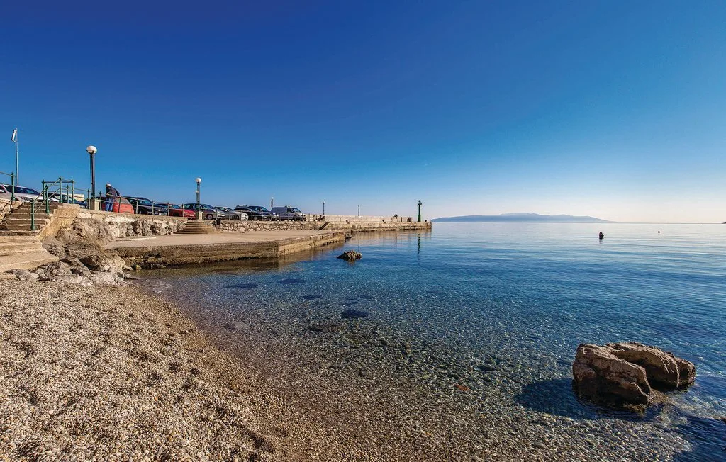 A clear shoreline with a rocky beach and calm blue water.