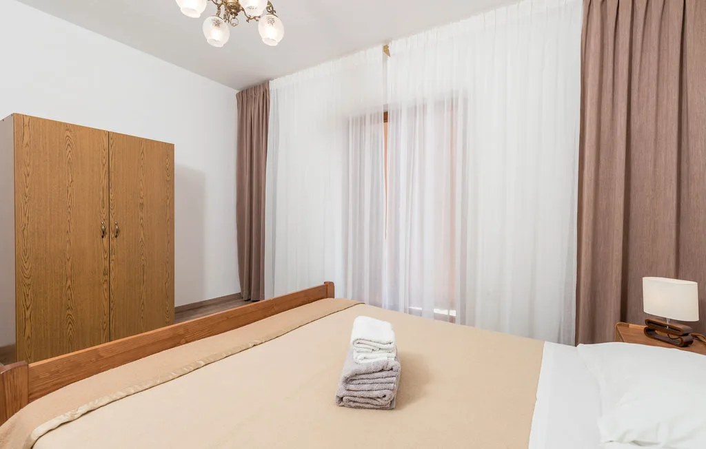 A bedroom with a bed, folded towels, and curtains over the window.