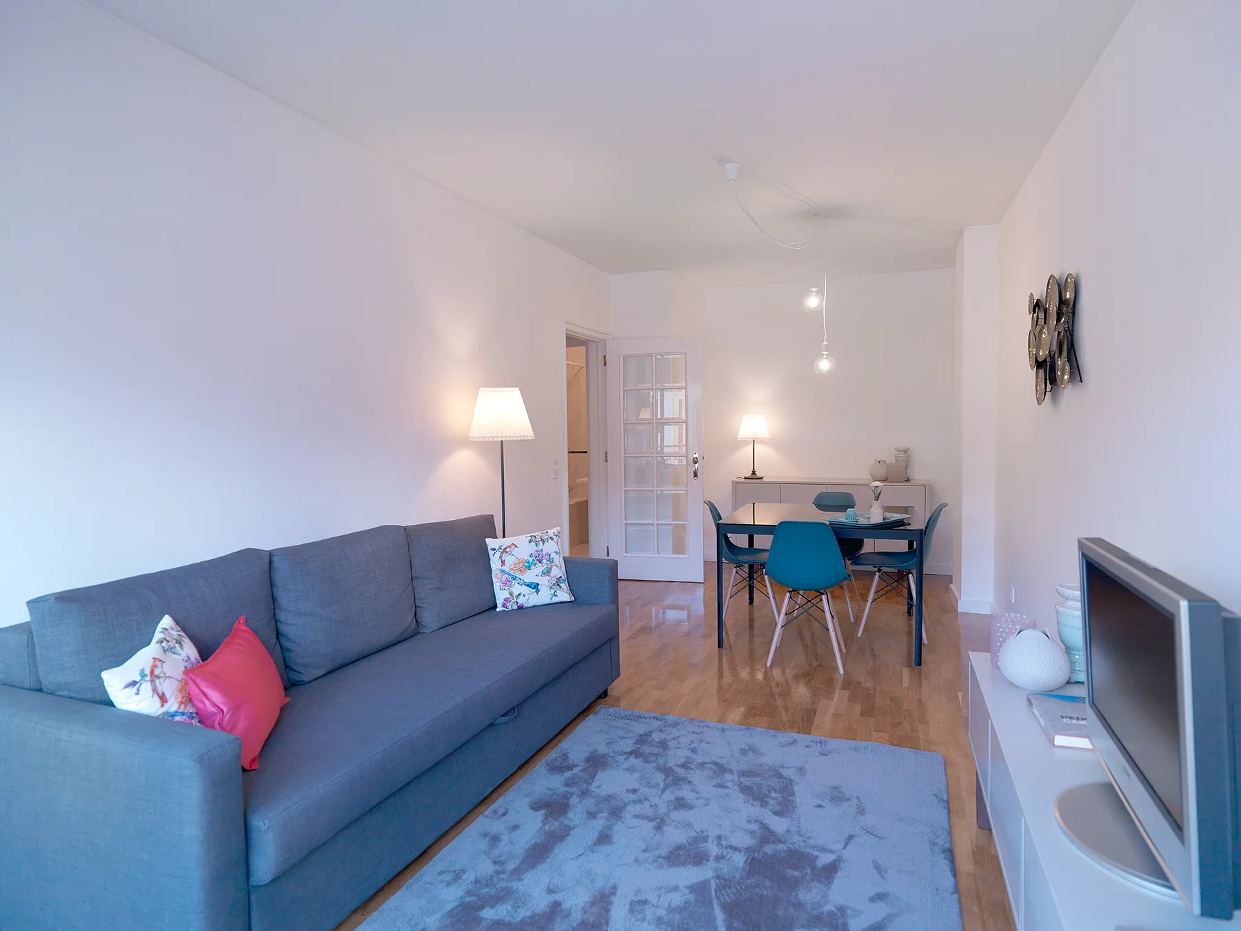 Una luminosa sala de estar y comedor con un sofá azul y una mesa.