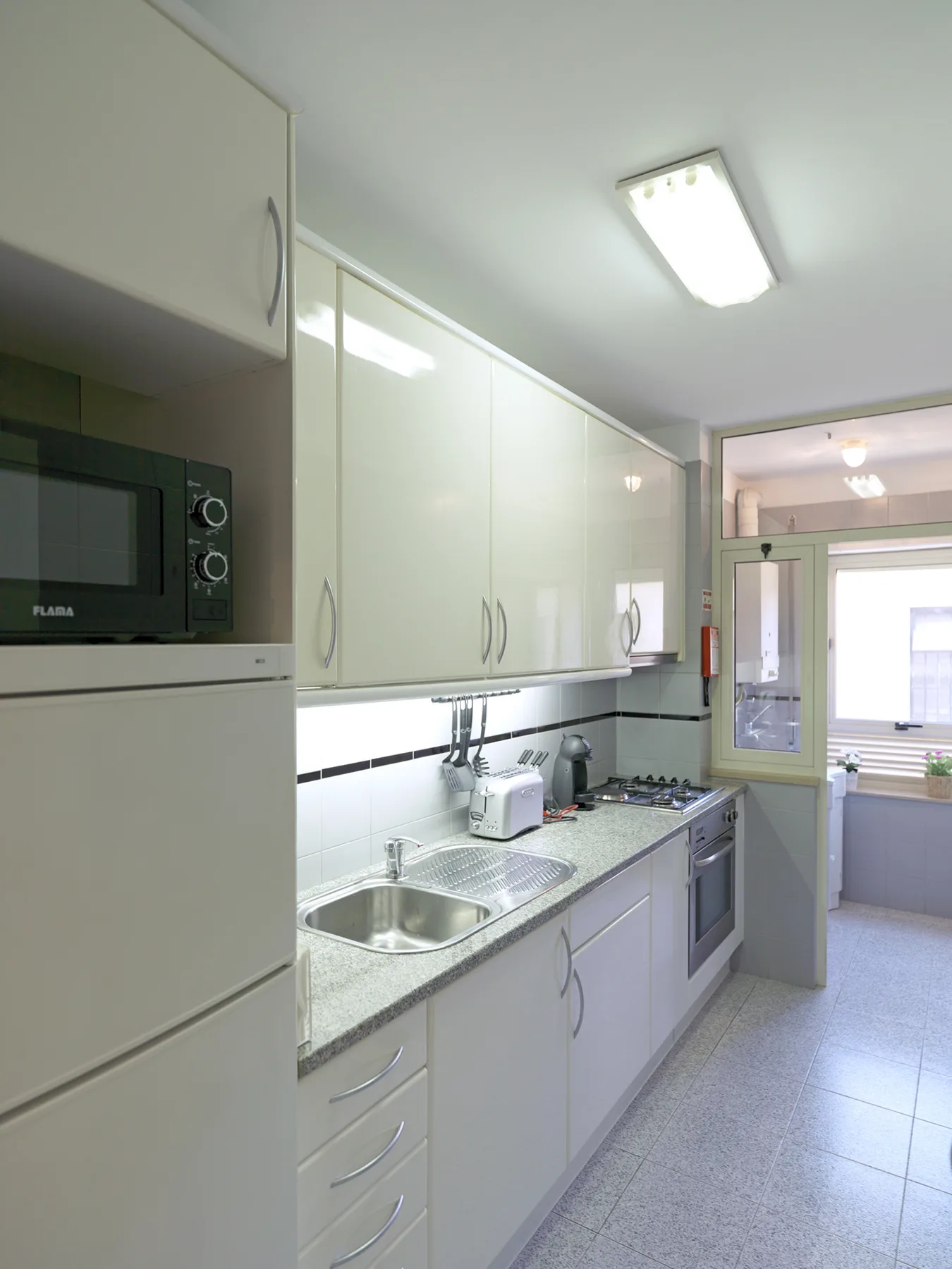 Una cocina luminosa con armarios blancos, encimera y electrodomésticos integrados.