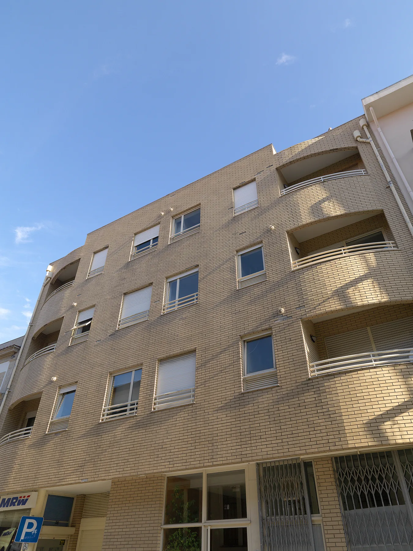 Un edificio de apartamentos de ladrillo con balcones bajo un cielo azul despejado.