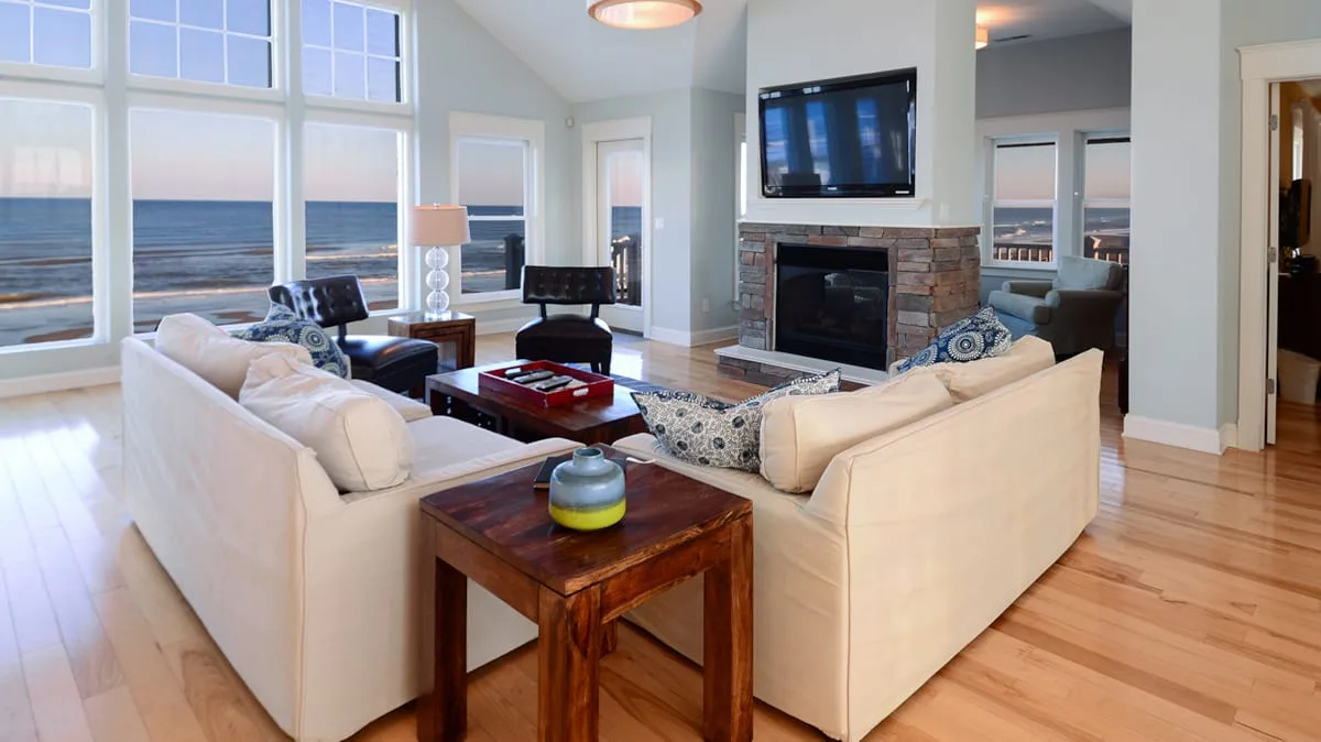 A bright living room with seating arranged around a fireplace and large ocean-facing windows.