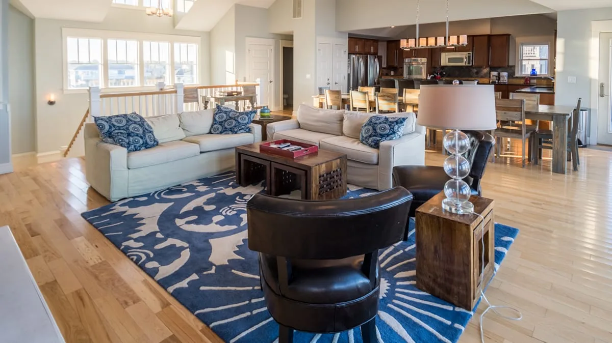 A bright open-plan living room with seating around a coffee table and kitchen beyond.