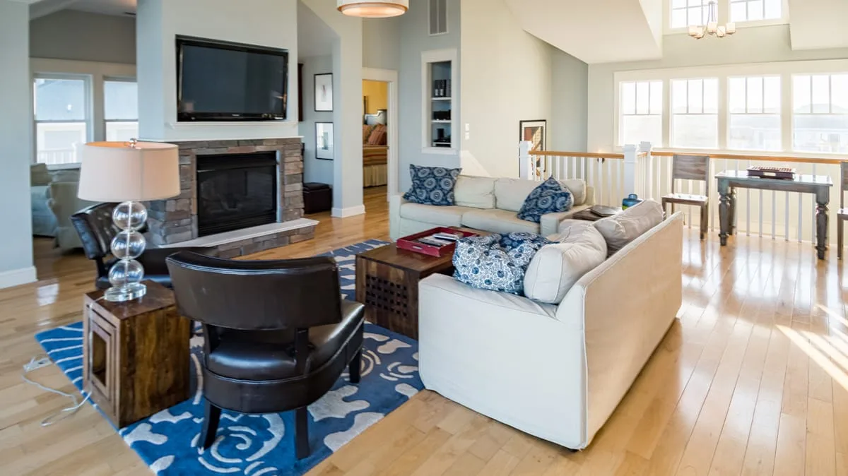 A bright open-plan living room with seating, a fireplace, and large windows.