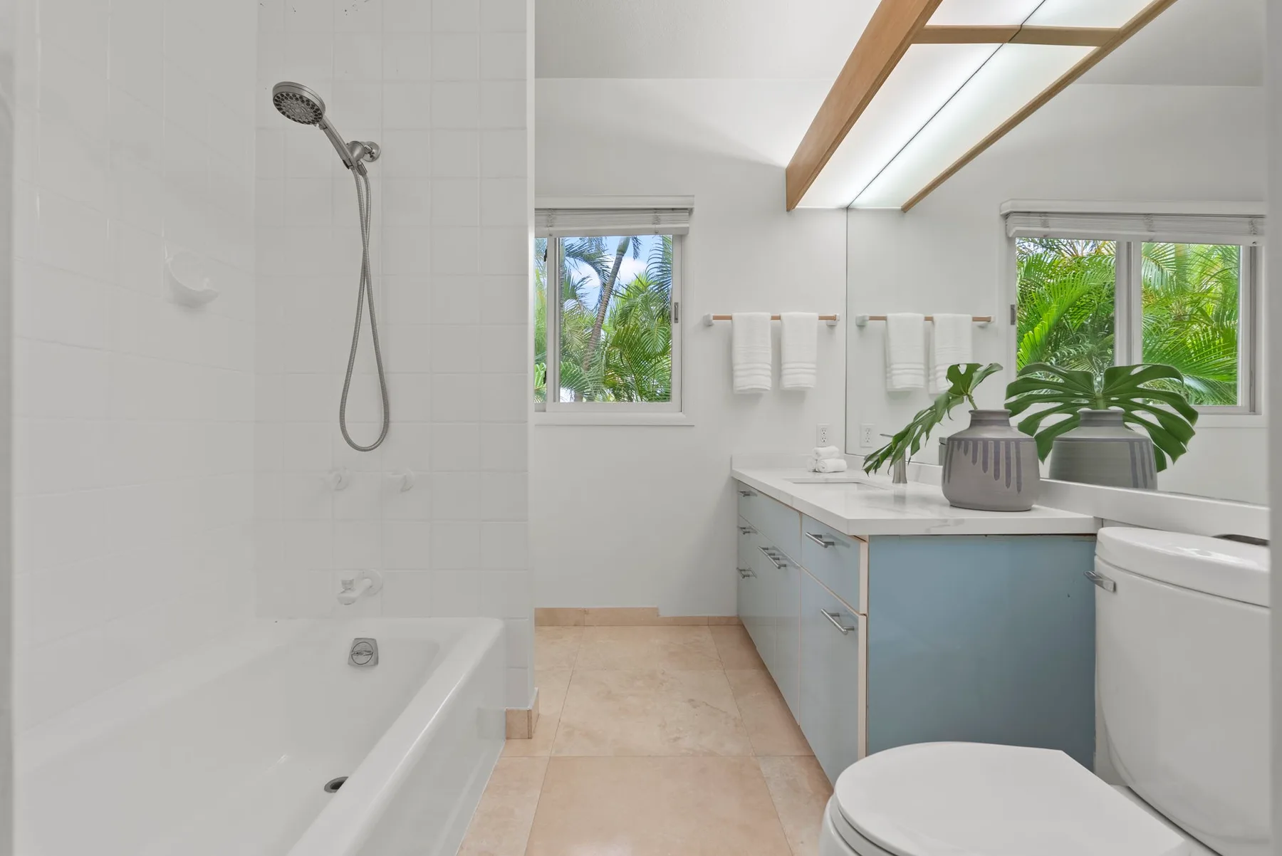 A bright bathroom with a bathtub, shower, vanity, and windows overlooking greenery.