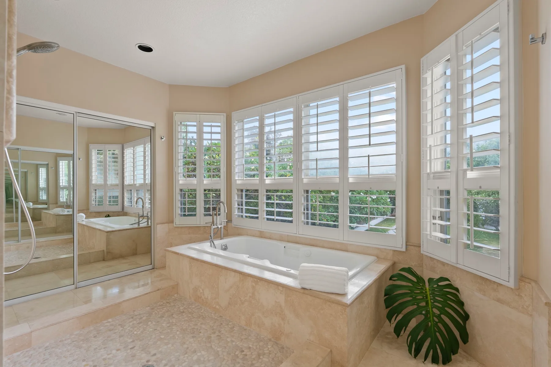 A bright bathroom features a built-in bathtub beneath several shuttered windows.
