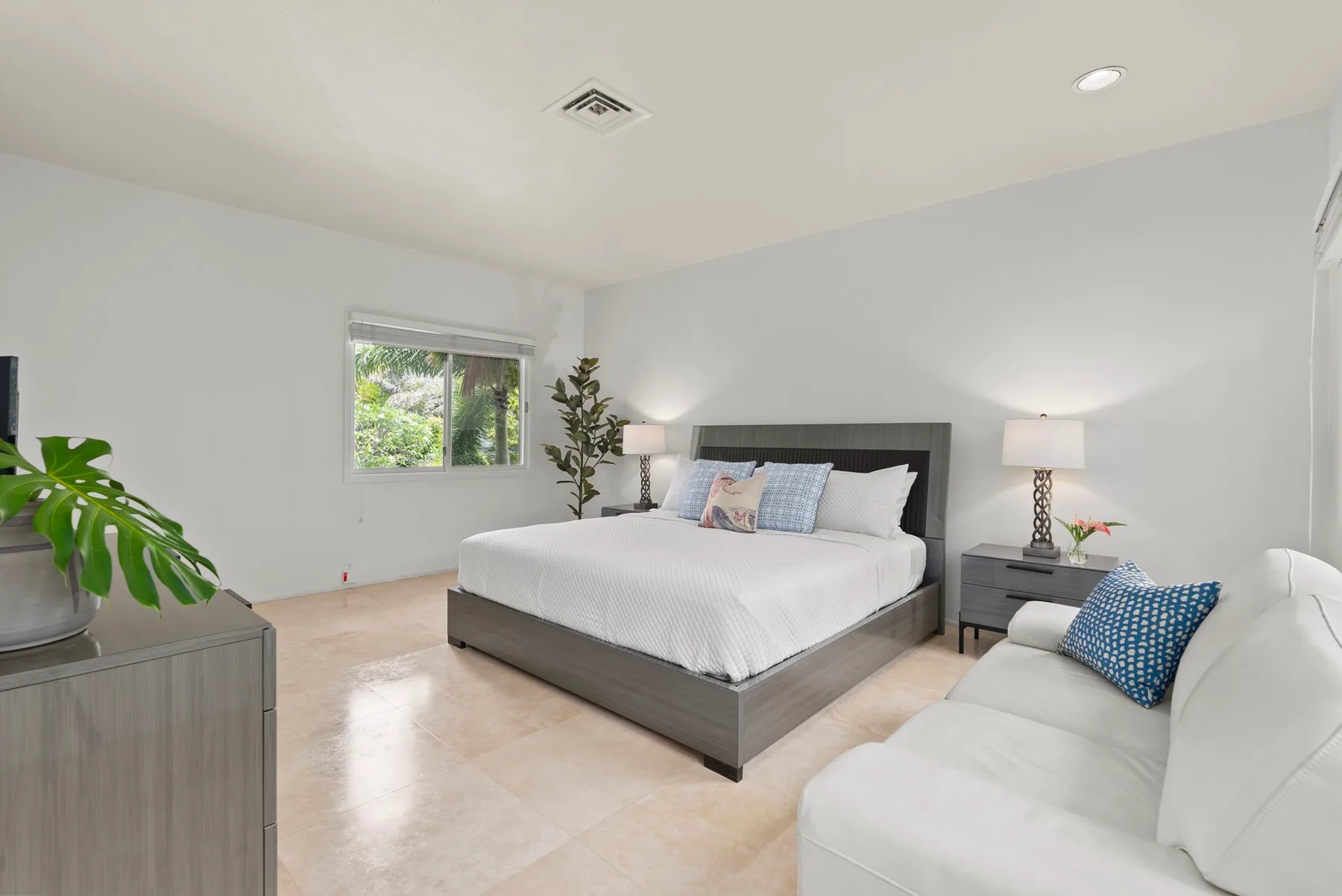 A bright bedroom with a large bed and a white sofa.