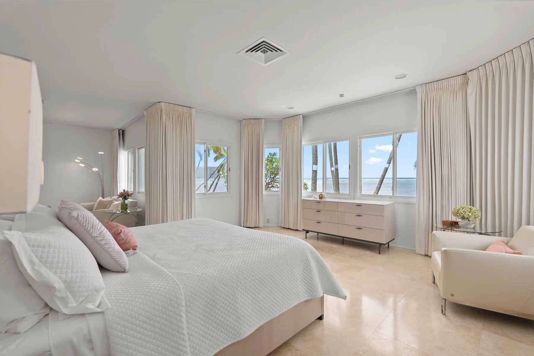 A bright bedroom with a large bed, dresser, and windows overlooking the water.