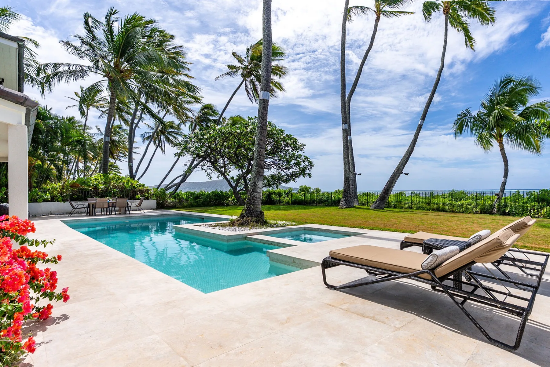 A swimming pool and lounge seating sit beside a palm-lined lawn.