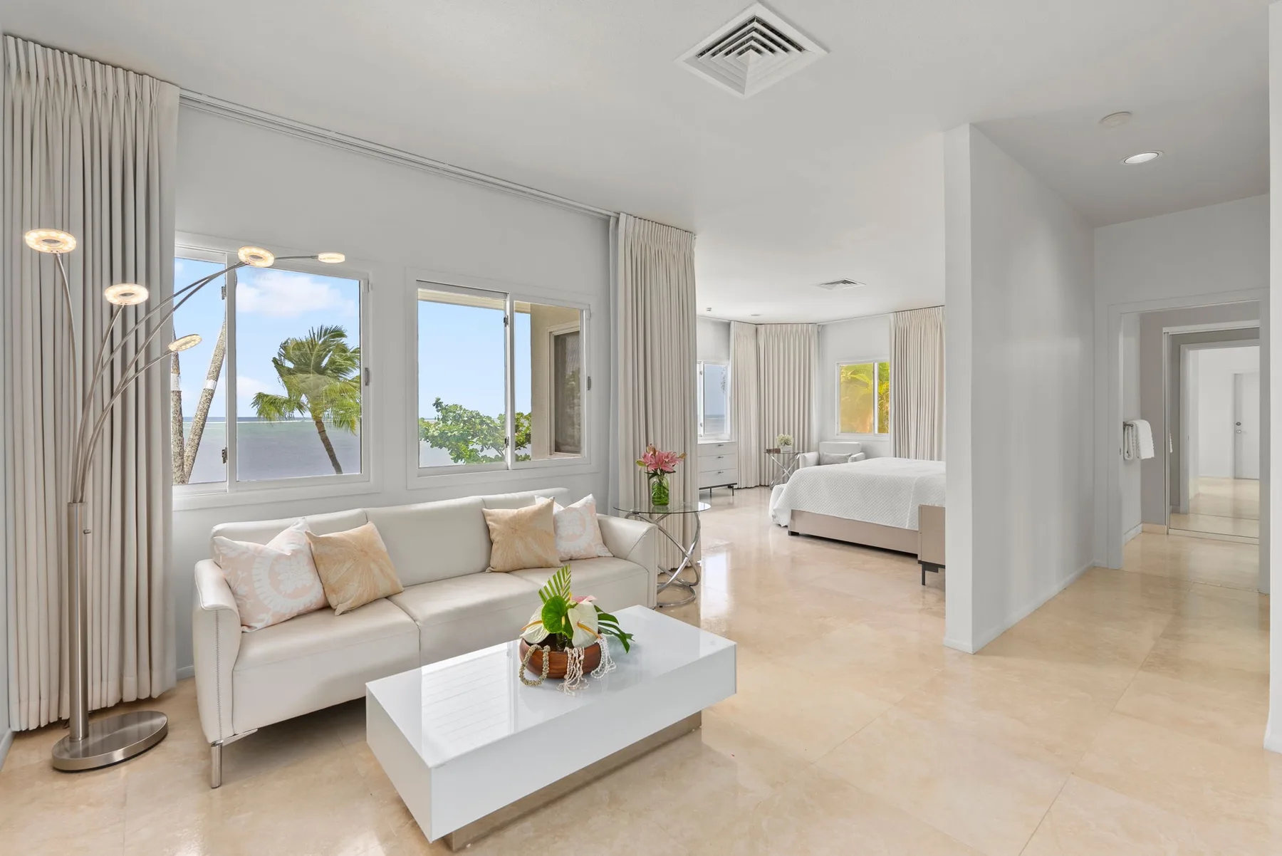 A bright living area with seating and a bedroom visible beyond.
