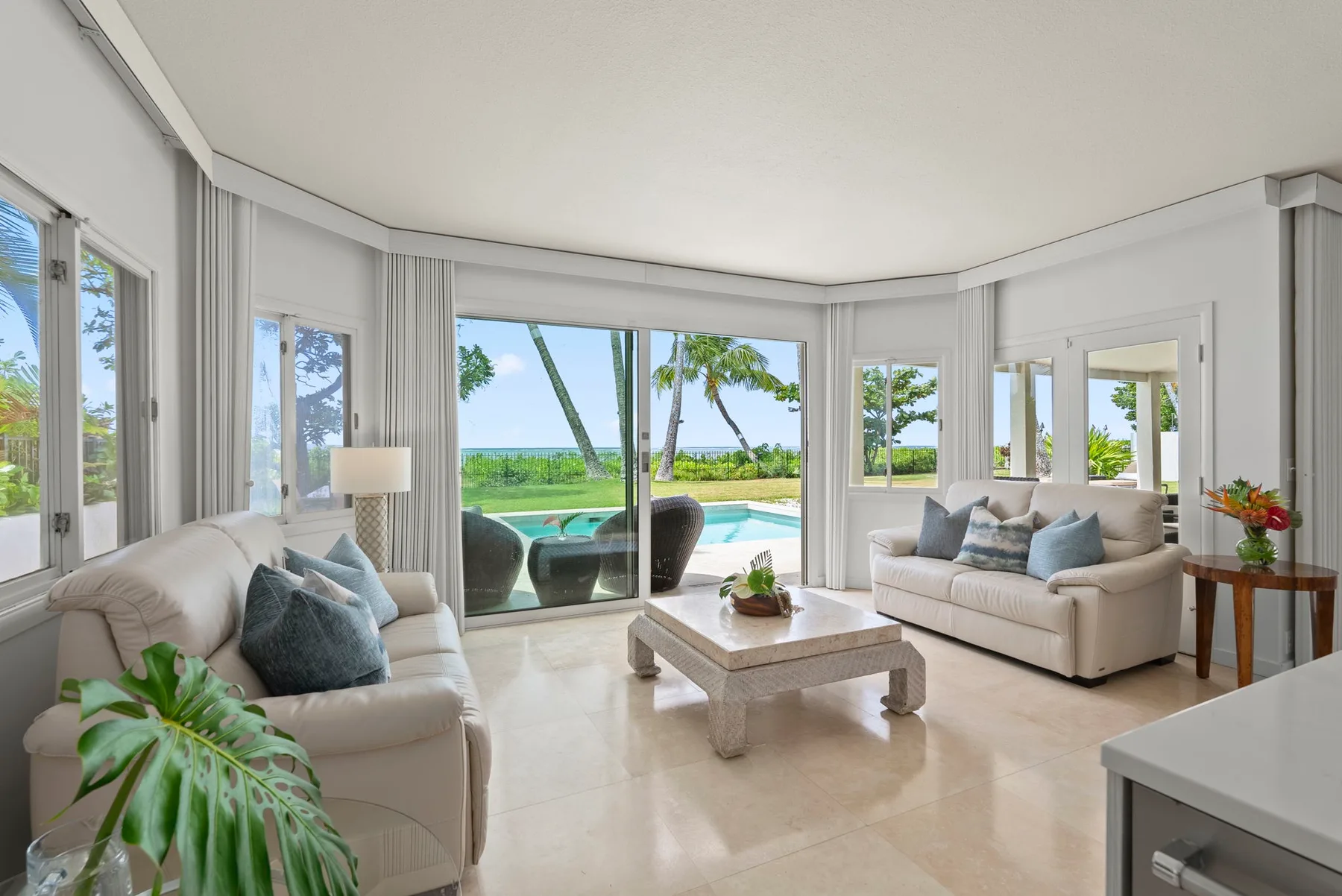 A bright living room with seating, a coffee table, and large windows overlooking a pool.