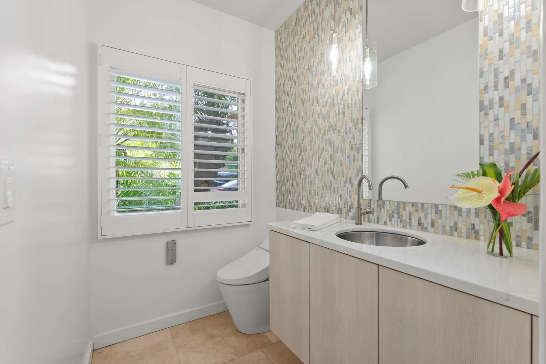 A bathroom with a vanity, sink, and toilet beneath shuttered windows.