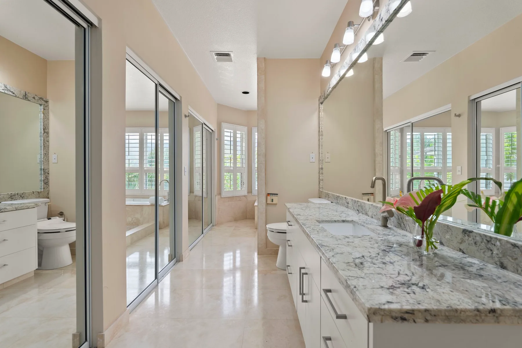 A bright bathroom with a long vanity, mirrors, and windows.