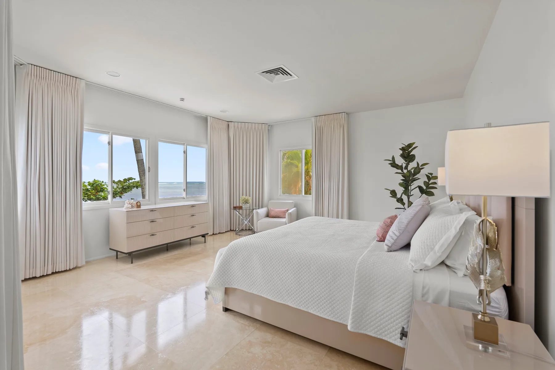 A bright bedroom with a bed, bedside lamp, and large windows.