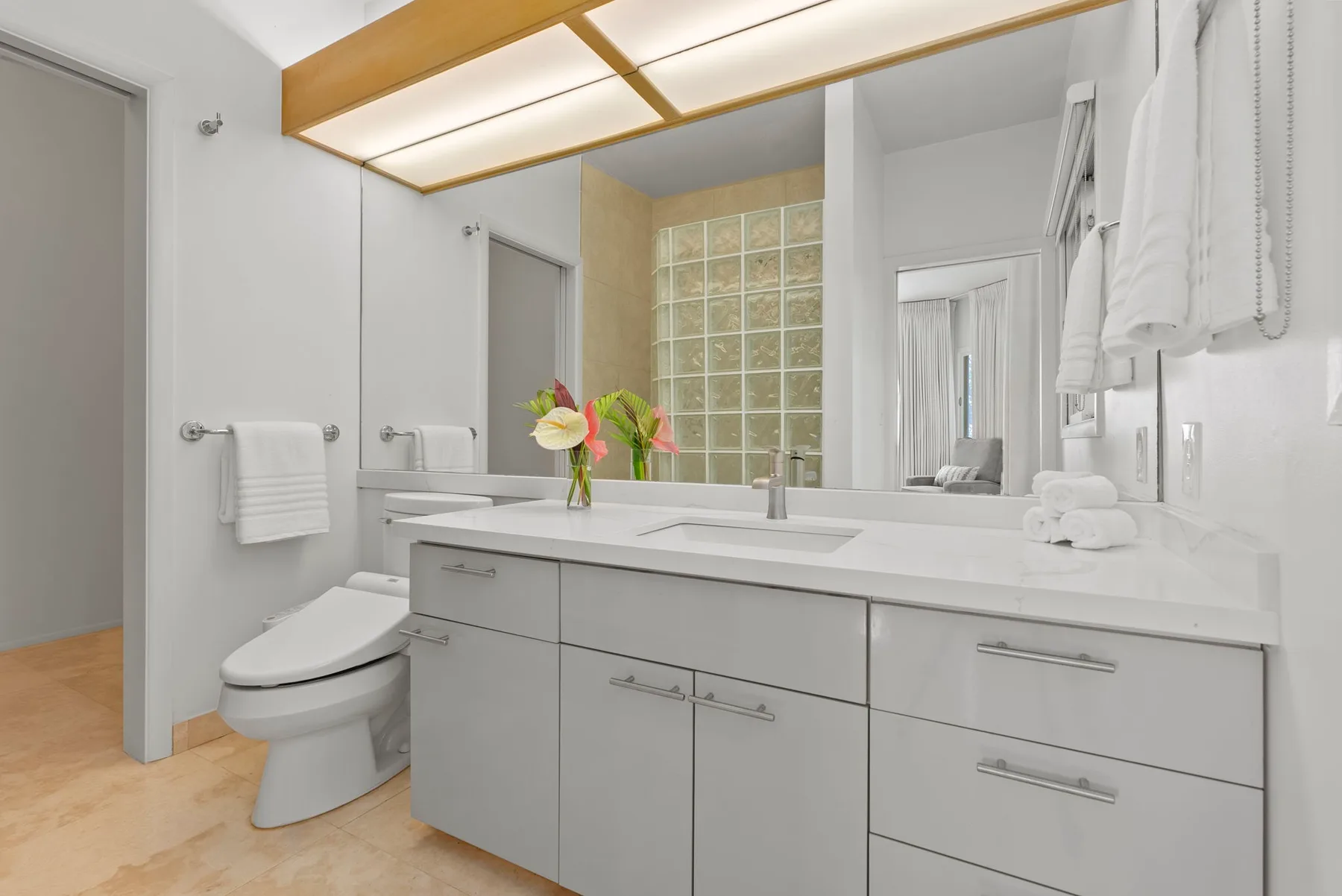 A bright bathroom with a long vanity, mirror, and toilet.