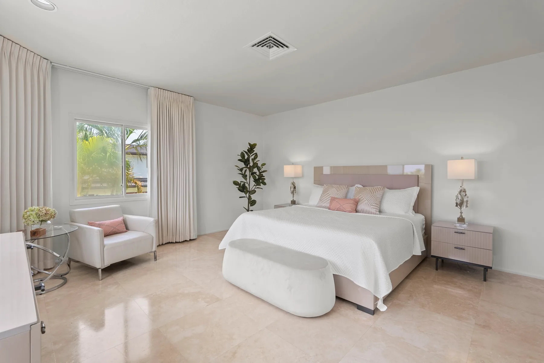 A bright bedroom with a bed, bedside tables, and a window with curtains.