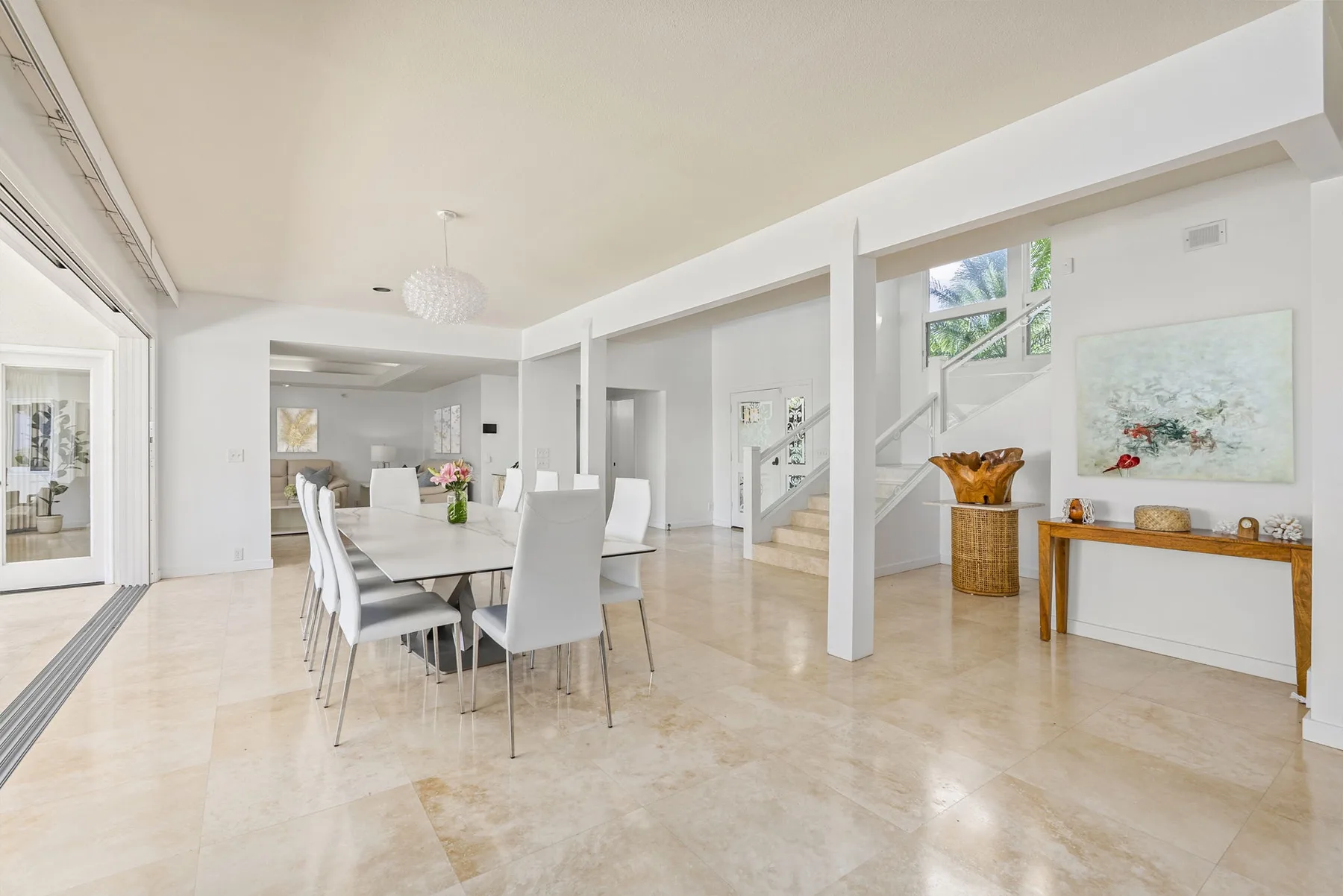 A bright dining area with a long table and chairs beside a staircase.